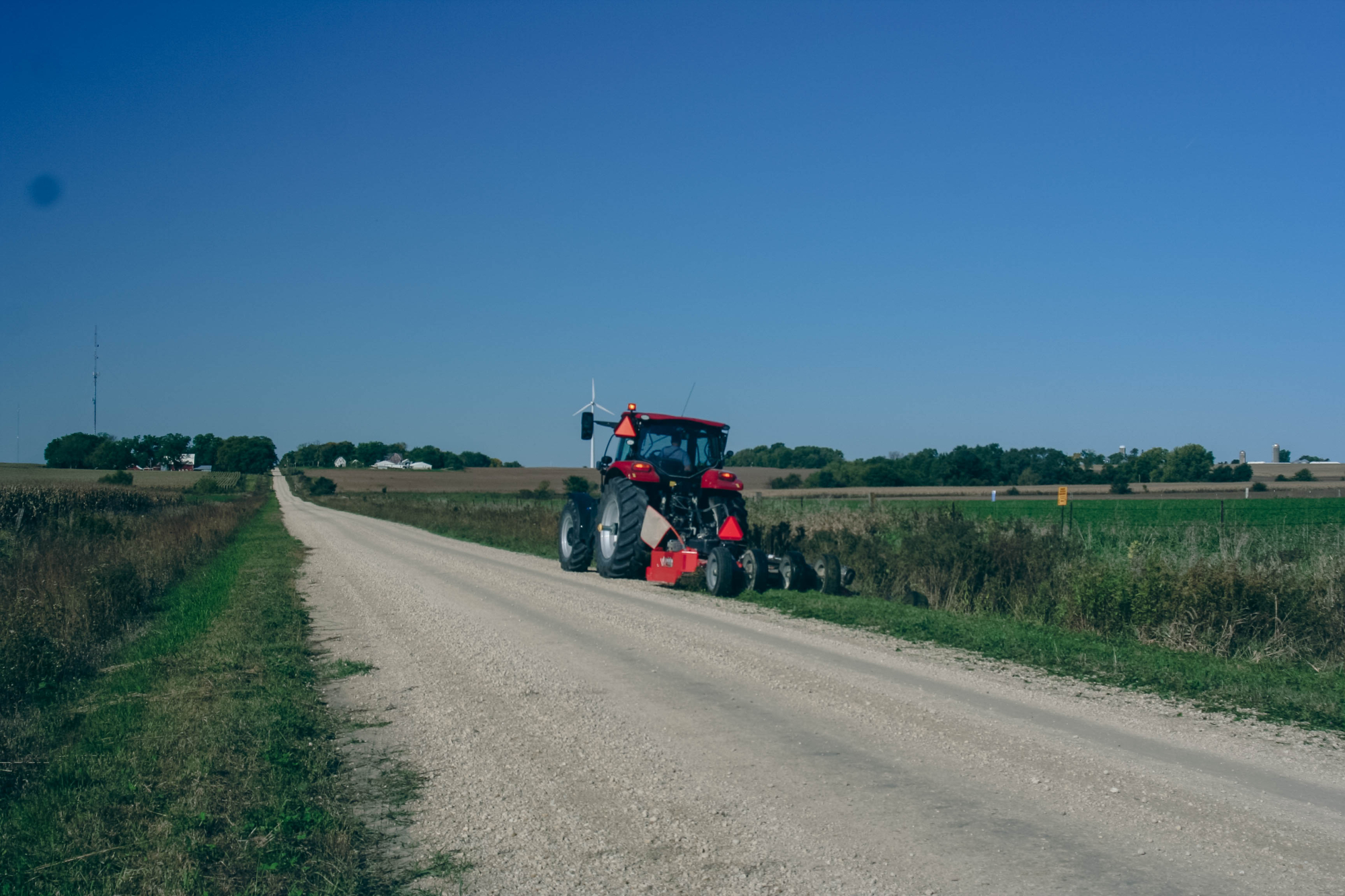 A tractor tends to roadside vegetation by a gravel road on a cloudless day.