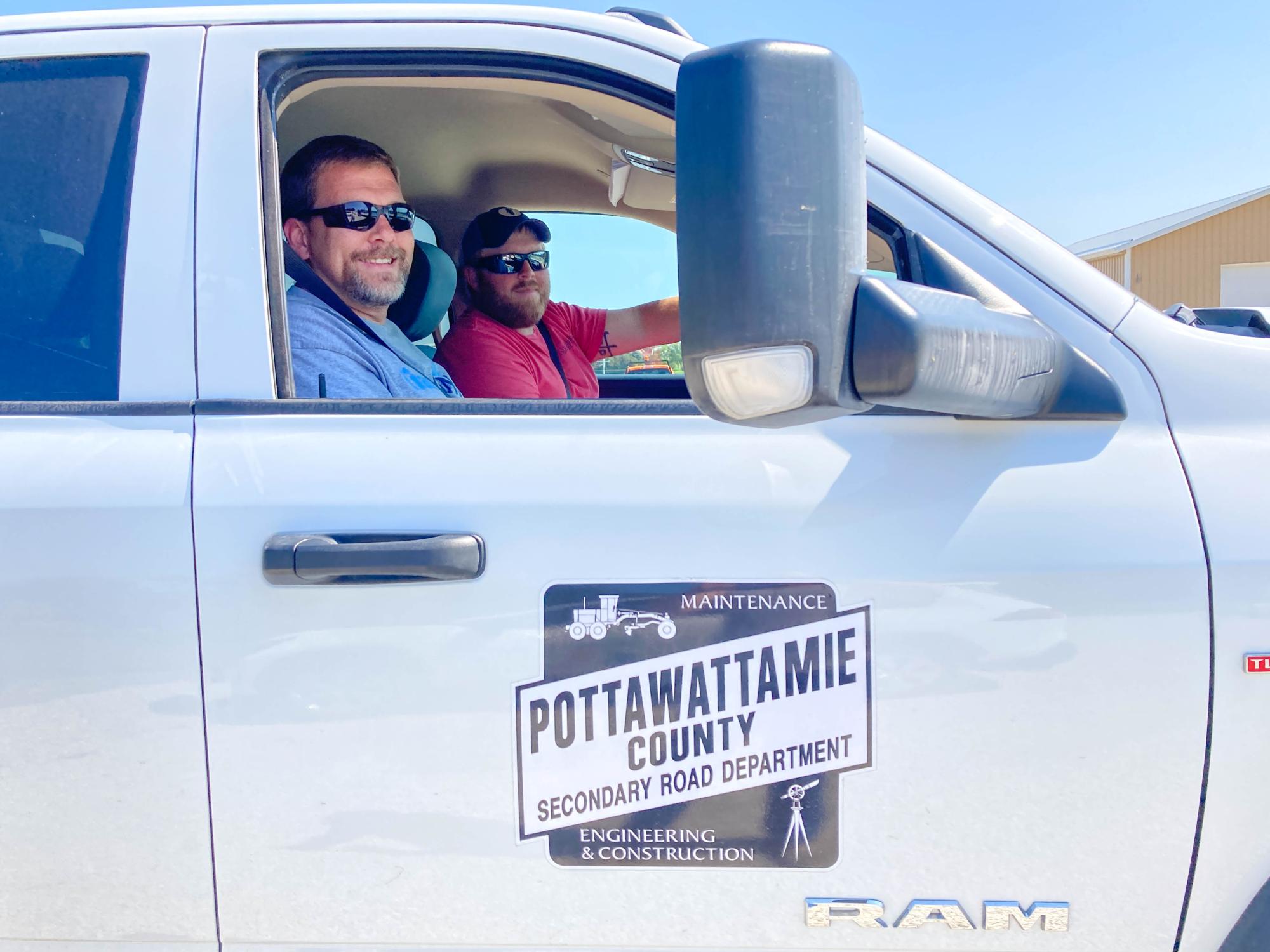 Two roadside management staff members smile while sitting  in a pickup truck.
