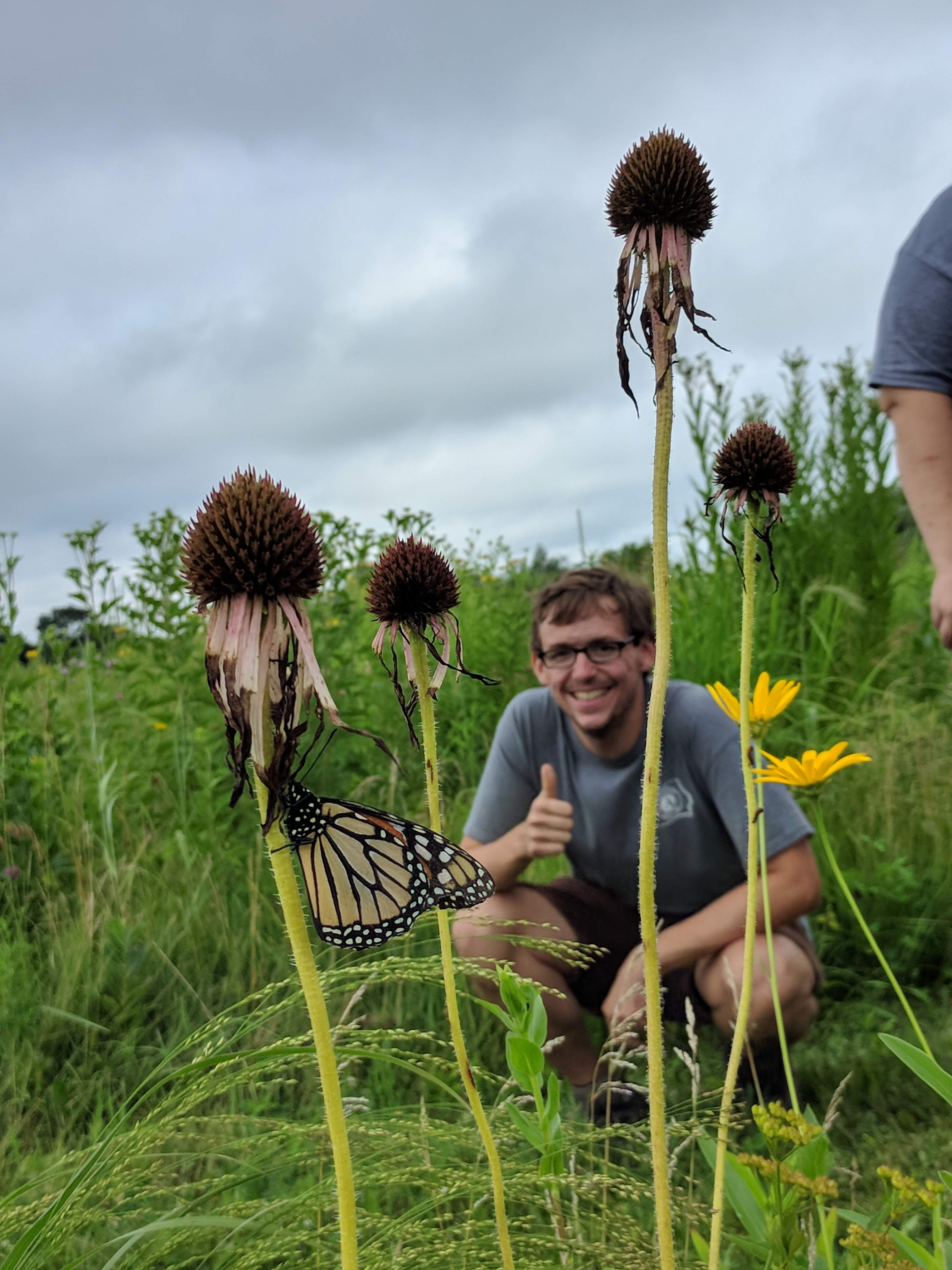 AmeriCorps member photographed with a monarch resting on pale purple cone flower